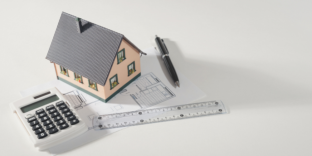 A toy house sits on a table with a pen and a calculator beside it.
